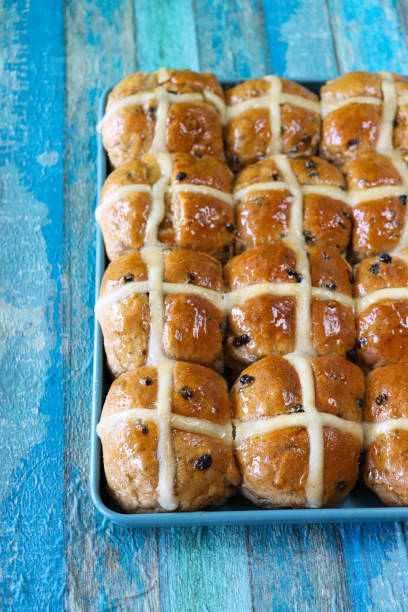 Image of freshly baked homemade Easter hot cross buns on blue baking tray on blue wooden table, home baking concept, focus on foreground, elevated view stock photo