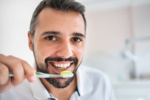 Close-up of a smiling man brushing his teeth with a toothbrush in the mirror of a dentist's office