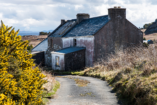 Abandoned property or house on Arranmore island, Republic of Ireland, County Donegal. Countryside forsaken villa with pitched roof. Derelict or destitute home shows Irish rural depopulation problem - Arranmore island, County Donegal, Republic of Ireland