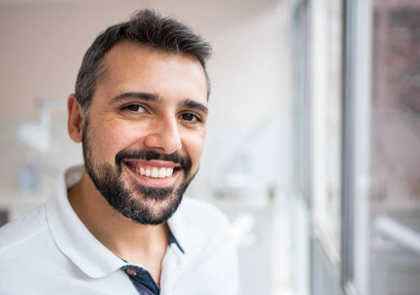 istock Smiling male dentist standing by a window in his office 1483018569