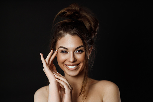 Beauty portrait of a smiling young woman with long brown hair, studio shot in front of back background