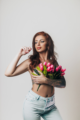 Portrait of a beautiful young woman covered in flowers wearing blue jeans, studio photoshoot in front of white background