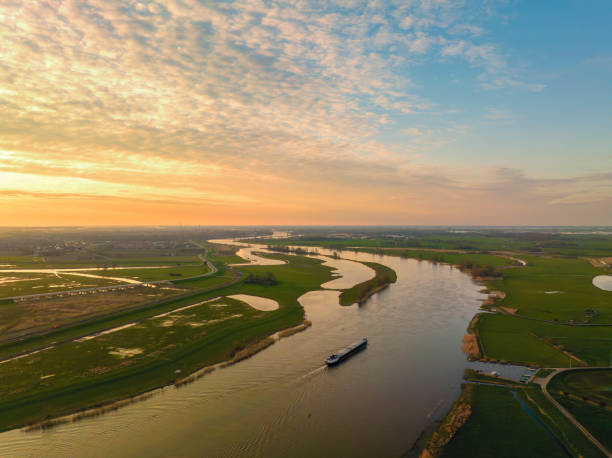 Ship sailing on the river IJssel during sunset panoramic bird's eye view Panoramic aerial view on a freight ship sailiing on the river IJssel during a springtime sunset in Overijssel. The flow of the river is leading towards the setting sun in the distance while lights are popping up in the city at the end of a beautiful springtime day. ijssel stock pictures, royalty-free photos & images