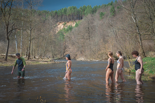 Vilnius, Lithuania - March 26 2023: Group of girls preparing for ice bathing together in cold water of a river with instructor. Wim Hof Method, cold therapy, breathing techniques, yoga and meditation