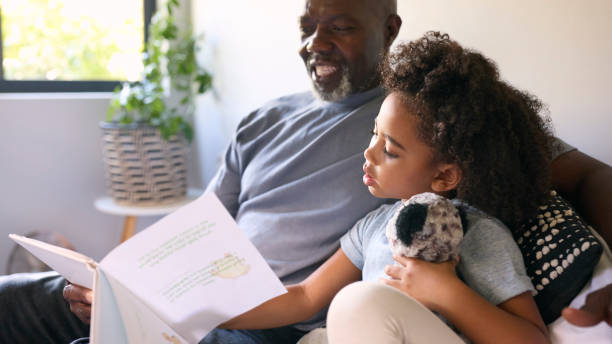 istock Grandfather Sitting On Sofa At Home Reading Book With Granddaughter 1483025644