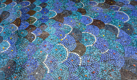 Dry mosaic bottom of an ancient fountain. Multi-colored mosaic tiles on the fountain pond without water. Pattern with texture of scales.