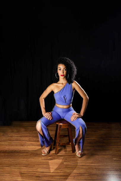 jeune femme vêtue d’une tenue bleue assise sur un tabouret en bois. - wall indoors chair floor photos et images de collection