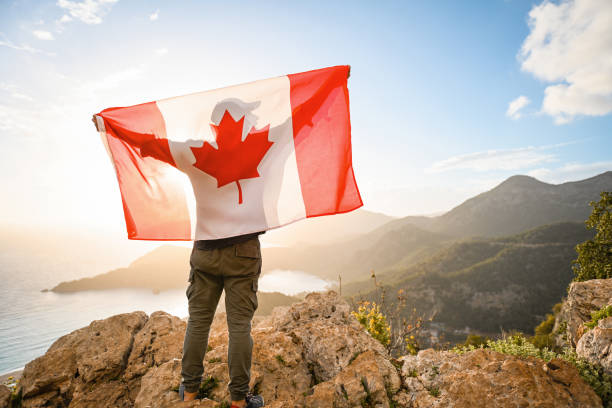 mann mit kanadischer flagge auf dem hintergrund des meeres und der berge - canadian flag canada flag freedom stock-fotos und bilder