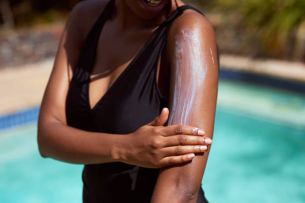 Close up of Black woman spreading sunscreen onto arm with pool background Close up of Black woman spreading sunscreen onto arm with pool background. High quality photo suntan lotion stock pictures, royalty-free photos & images