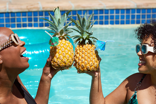 Close up of pineapple drink with two friends drinking in the pool, summer fun. High quality photo