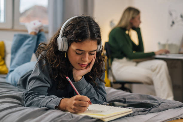 students in dorm room female student with headphones does homework in dorm room roommate stock pictures, royalty-free photos & images