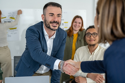 Handshake between colleagues, young casual and modern businessman shaking hands for the positive result of the contract with a mature woman manager, making successful deal