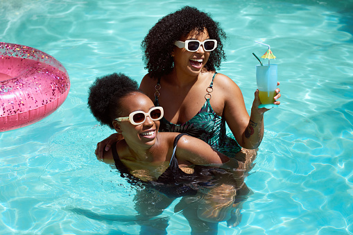 Two Black friends having fun in the pool, piggyback swimming laughing having fun. High quality photo