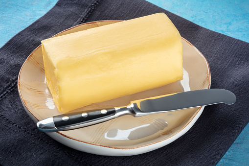 A stick of fresh butter with a knife on a plate, on a blue background, cooking ingredient