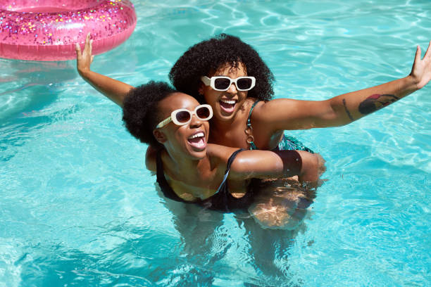 Two Black friends having fun in the pool, piggyback swimming laughing having fun