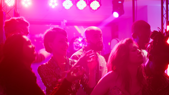 Diverse people having fun at nightclub, dancing and partying together on live music in discotheque. Cheerful friends clubbing and jumping around on dance floor, party discolights.