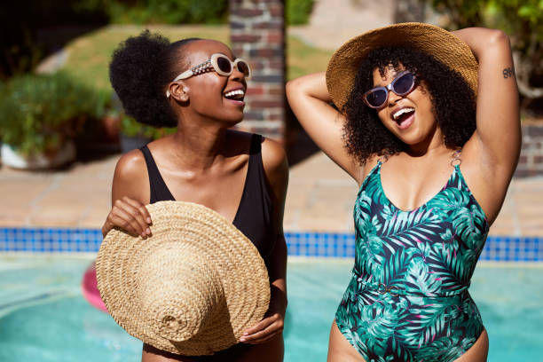 Two young friends pose and laugh with straw hats at the swimming pool summer fun