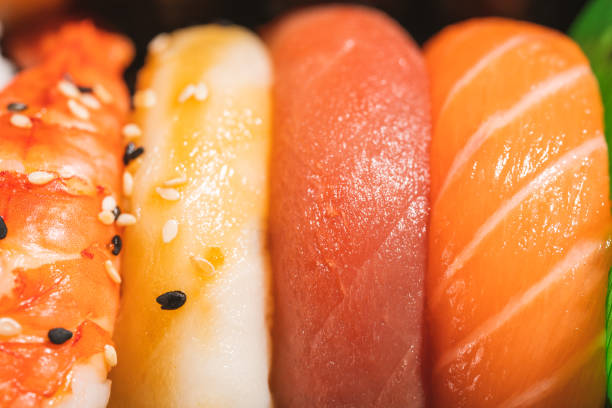 Close up of nigiri sushi with salmon, tuna, prawn in a take away container.\nSake nigiri, majuro nigiri, ebi nigiri.