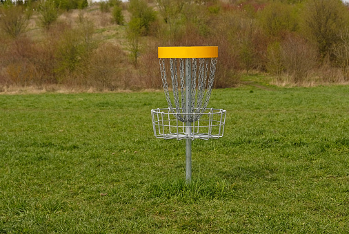 Disc Golf basket. Frisbee golf is sport and hobbie in outdoor park. Metal basket with chains for disc game surrounded by vibrant green trees.