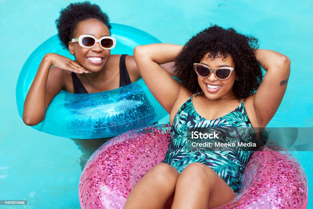 Two young Black friends float in inflatable rings in pool, swimming having fun Two young Black friends float in inflatable rings in pool, swimming having fun. High quality photo Swimming Pool Stock Photo