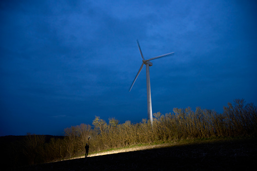 Renewable energy. Man checking up on windmill at night with lamp.