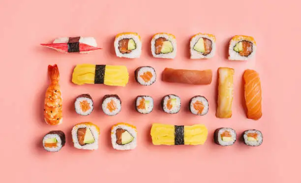 Photo of Food knolling concept - top down view of various nigiri sushi and sushi rolls on pink background