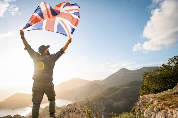 mann mit der englischen flagge auf dem hintergrund des meeres und der berge - english flag british flag flag british culture stock-fotos und bilder