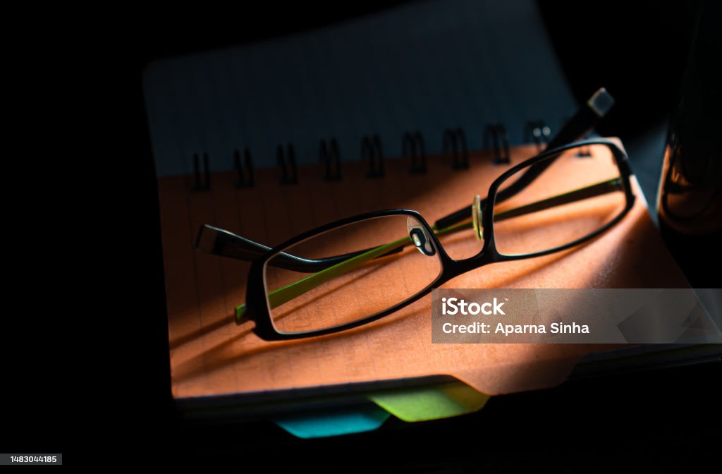 Eyeglasses on table above the daily planner book with sunset shadow background Black Color Stock Photo