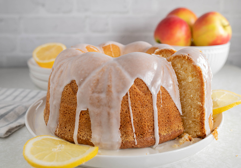 Delicious homemade bundt cake with lemon glaze. Served whole and slice with cross section view on white kitchen counter. Closeup, front view