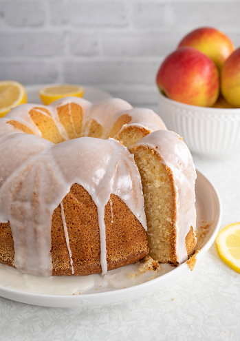 Delicious homemade glazed lemon cake or blond gugelhupf. Served whole and slice on white kitchen table background. Closeup, front view with copy space
