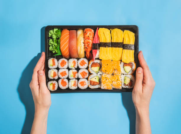 frau hält einen behälter zum mitnehmen mit sushi-set auf blauem hintergrund - sake nigiri stock-fotos und bilder