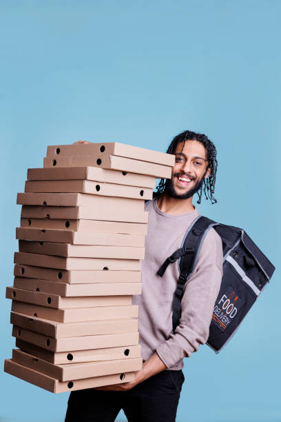 fattorino arabo spensierato che trasporta una grande pila di scatole di pizza - pizza box foto e immagini stock