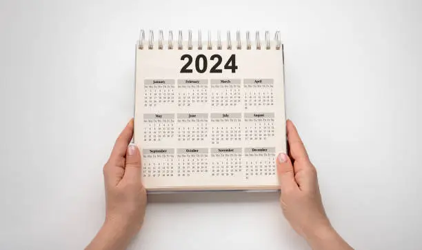 Photo of Hands hold Calendar Year 2024 schedule. 2024 desk calender notepad on wooden table and gray background. New Year. plans for 2024. white background