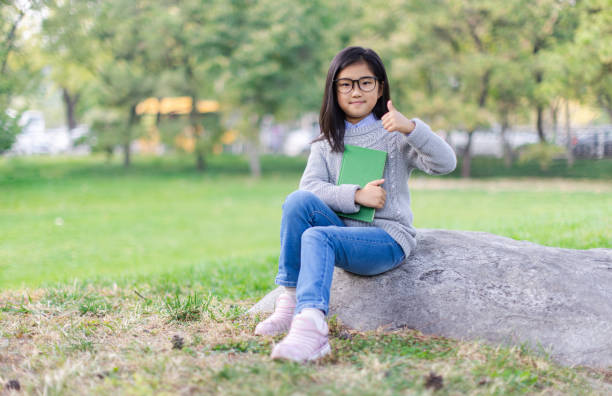 niña sentada con un libro sosteniendo y los pulgares hacia arriba - american sign language student learning real people fotografías e imágenes de stock