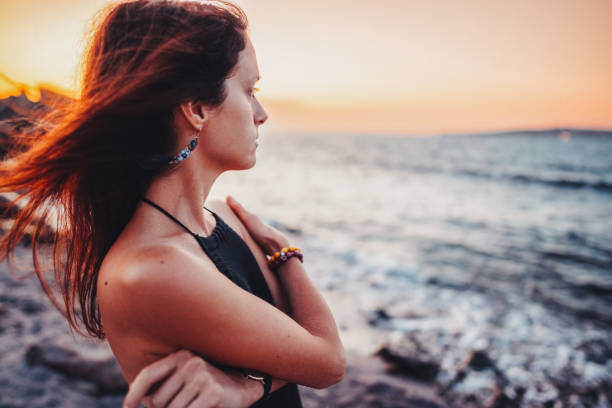 mujer en la orilla del mar mirando la puesta de sol - piel de gallina fotografías e imágenes de stock