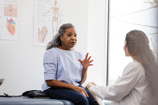 The senior adult woman gestures while talking to her doctor about an upcoming procedure she needs for her ear.