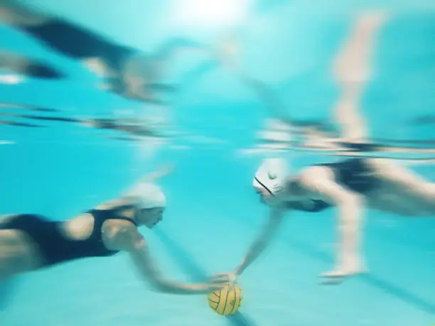 Water polo, sports and women underwater for a ball during a competition, game or swimming. Teamwork, action and blurred athlete team playing a professional match in a pool for a championship