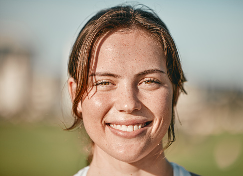 Portrait, happy and smile with a woman outdoor on a bokeh green background for carefree positivity. Face, wellness and zoom with an attractive young female standing outside on a summer day in nature