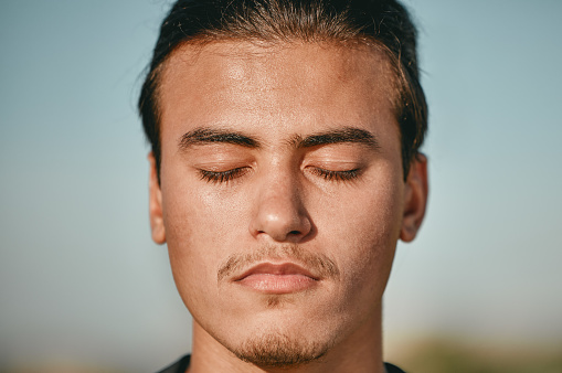 Zen, meditation and face of man meditating closed eyes outdoors for calm, peace and is mindful with blue sky background. Person, relax and spiritual male with faith in wellness and health
