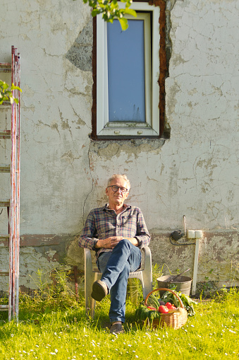 Senior man sitting on chair in front of house wall.