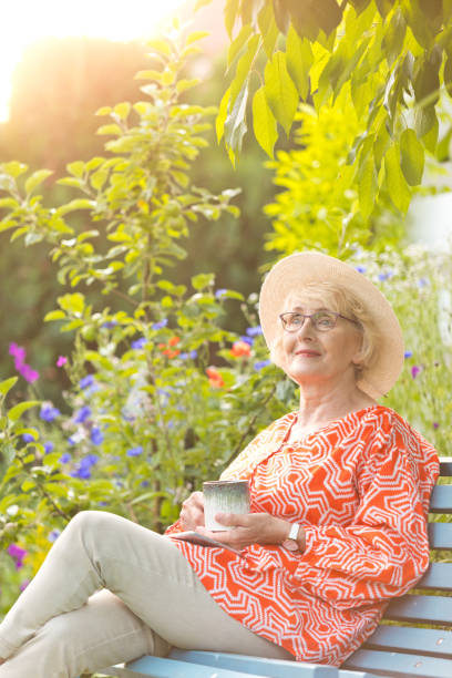 istock Smiling senior woman with cup sitting on bench in garden 1483055610