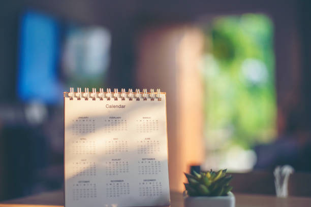 istock Desktop calendar, clock, and cactus placed on student wooden desk. calender for planner to plan daily appointments each day, month, and year on wooden table. Calendar background concept. 1483057164
