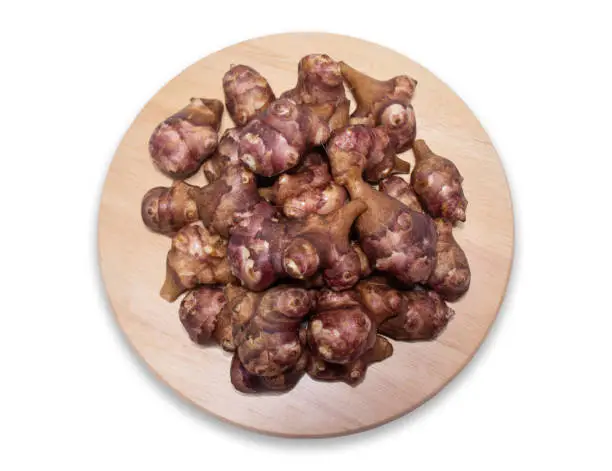 Jerusalem artichoke on a round wooden cutting board isolated on a white background with clipping path.
