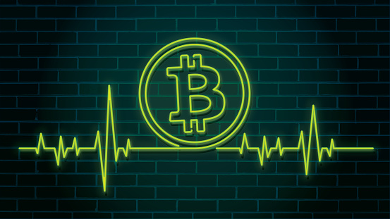 Heartbeat pulse shaped green illuminated neon Bitcoin sign on a brick wall