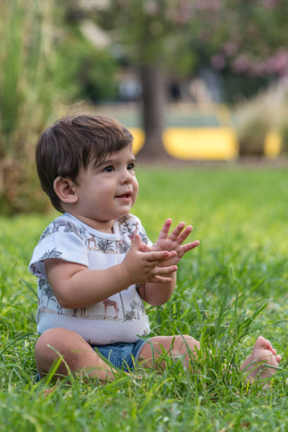 istock Cute baby clapping and playing while sitting on the grass in a park. 1483058967