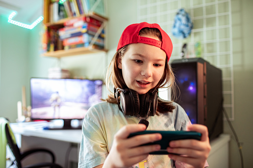 Close up of a Young girl playing games on her smart phone in her bedroom by the desktop computer