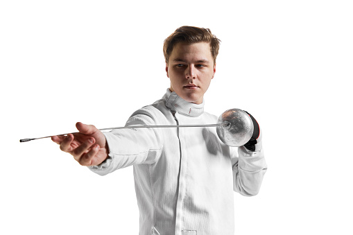 Young man, male fencer in fencing costume mask standing with sword over white studio background. Sport, motivation, professional skills. Copyspace for ad, text.