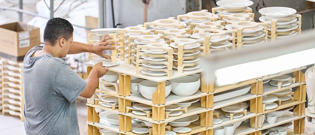 Young man arranging newly made pottery plates on drying rack in ceramic factory