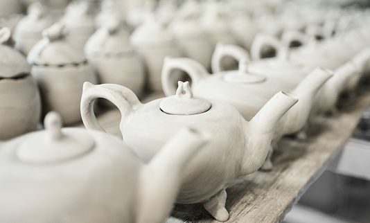 Large number of handmade clay teapots drying on rack at ceramic manufacturing factory