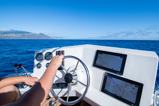 Unrecognizable sailor driving a fishing boat in the ocean.